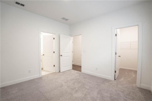 unfurnished bedroom featuring a walk in closet, ensuite bathroom, light colored carpet, and a closet