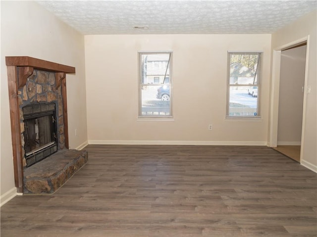 unfurnished living room featuring a textured ceiling, a stone fireplace, and dark hardwood / wood-style floors