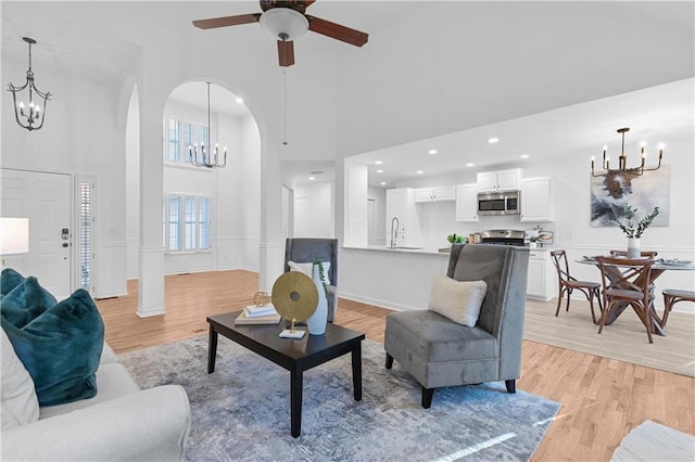 living area with arched walkways, ceiling fan with notable chandelier, light wood-type flooring, and a towering ceiling