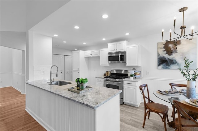 kitchen featuring light stone countertops, appliances with stainless steel finishes, light wood-style floors, white cabinetry, and a sink