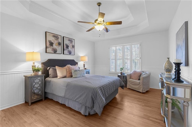 bedroom with a tray ceiling, wainscoting, and light wood finished floors