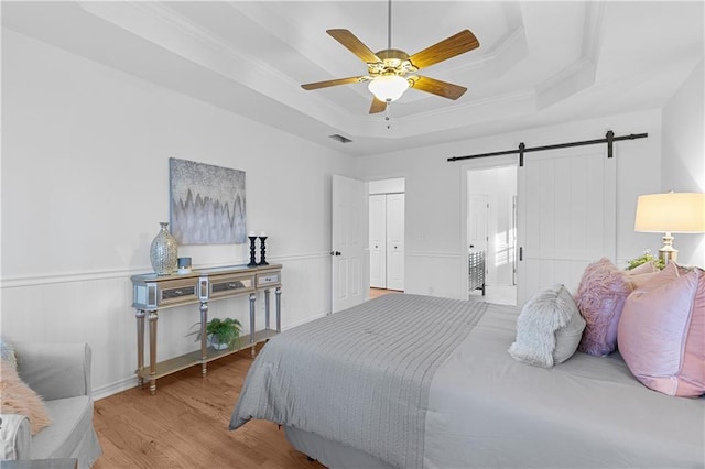 bedroom featuring visible vents, wood finished floors, a barn door, crown molding, and a raised ceiling