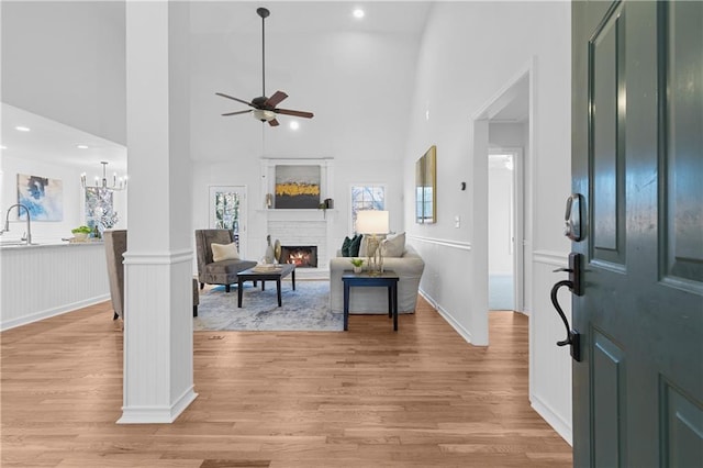 foyer with a lit fireplace, a wainscoted wall, ceiling fan with notable chandelier, and light wood-style floors