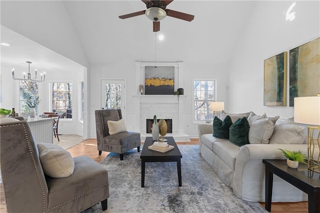 living room with high vaulted ceiling, wood finished floors, a fireplace, and ceiling fan with notable chandelier