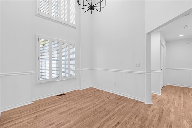 spare room with visible vents, wood finished floors, a wainscoted wall, and a chandelier