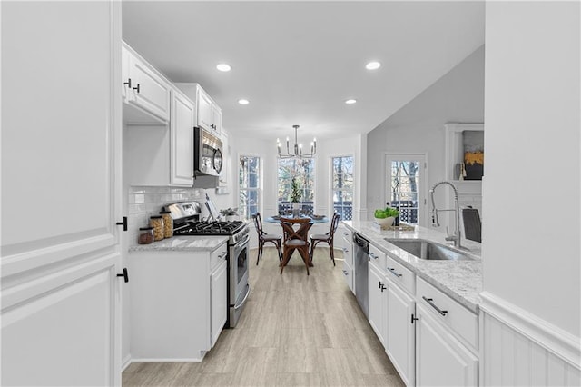 kitchen with a chandelier, light stone counters, white cabinets, stainless steel appliances, and a sink