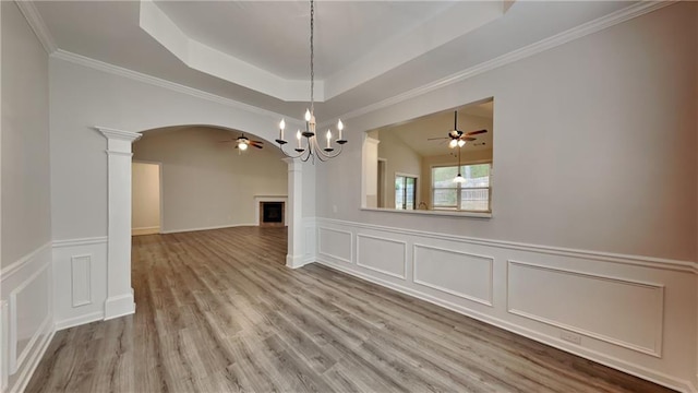 unfurnished dining area with ceiling fan with notable chandelier, light wood-type flooring, ornamental molding, a tray ceiling, and decorative columns