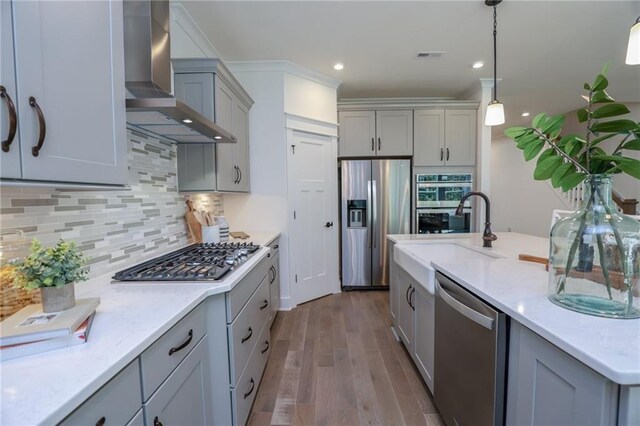 kitchen featuring gray cabinetry, wall chimney exhaust hood, stainless steel appliances, backsplash, and light hardwood / wood-style floors