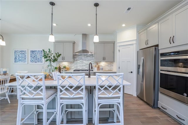 kitchen with pendant lighting, a kitchen breakfast bar, wall chimney range hood, decorative backsplash, and stainless steel appliances