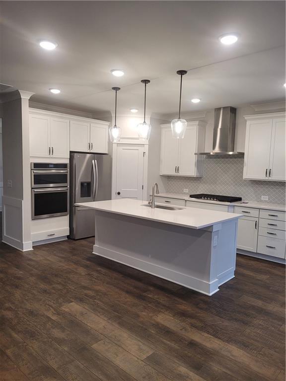 kitchen with wall chimney range hood, sink, decorative light fixtures, white cabinetry, and stainless steel appliances