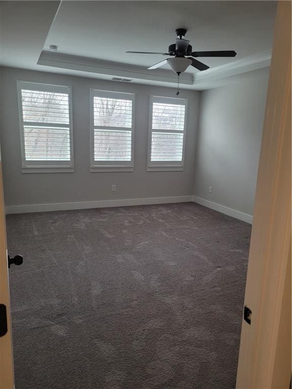 unfurnished room with a raised ceiling, ceiling fan, and dark colored carpet