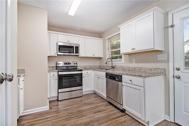 1829 Goddard St SE, Atlanta, GA 30315 - kitchen with appliances with stainless steel finishes, wood finished floors, white cabinetry, a textured ceiling, and light stone countertops