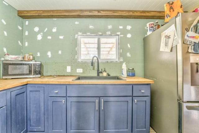 kitchen with a sink, beamed ceiling, wood counters, and stainless steel appliances