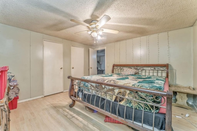 bedroom featuring a ceiling fan, wood finished floors, multiple closets, and a textured ceiling