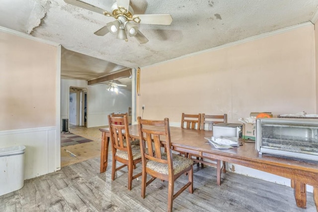 dining room with ceiling fan, a wainscoted wall, wood finished floors, and ornamental molding