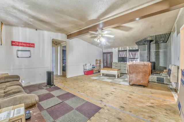 living room featuring lofted ceiling with beams, a textured ceiling, a wood stove, and ceiling fan