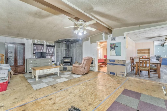 living area featuring a ceiling fan, vaulted ceiling with beams, a wood stove, and a textured ceiling