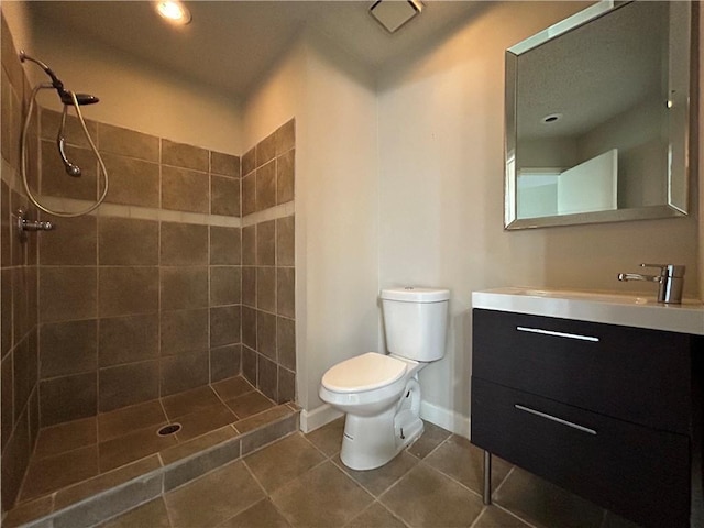 bathroom with tile patterned flooring, toilet, a tile shower, and vanity