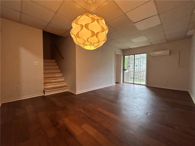 interior space featuring a paneled ceiling, an AC wall unit, and dark wood-type flooring