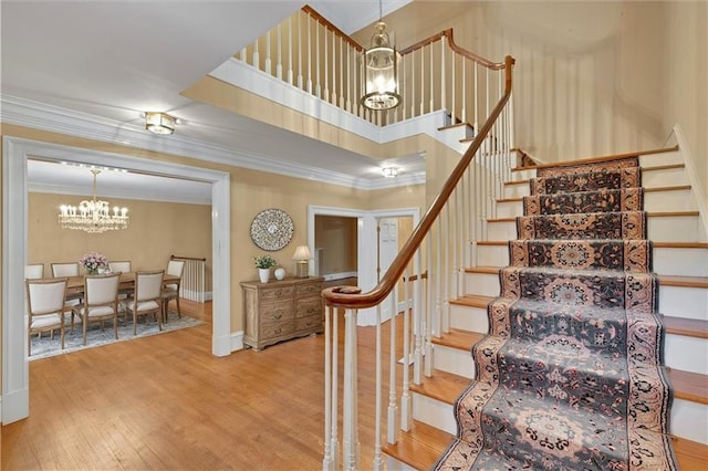 staircase featuring wood-type flooring, an inviting chandelier, and crown molding