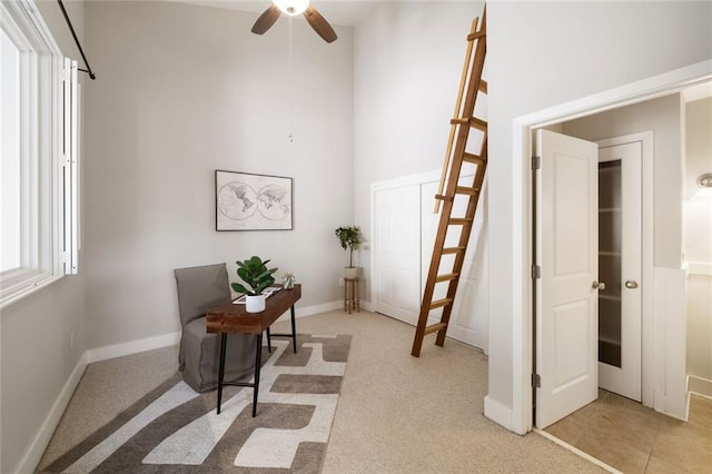 office space featuring baseboards, light carpet, a towering ceiling, and a ceiling fan