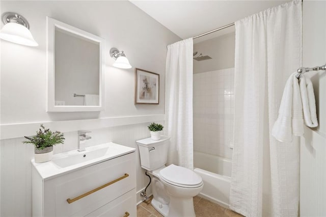 bathroom featuring vanity, a wainscoted wall, tile patterned flooring, shower / bath combination with curtain, and toilet