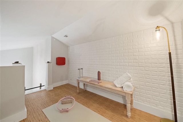 interior space featuring vaulted ceiling, wood finished floors, baseboards, and brick wall