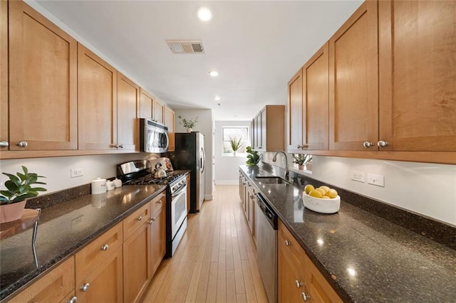 kitchen with visible vents, a sink, dark stone countertops, stainless steel appliances, and light wood finished floors