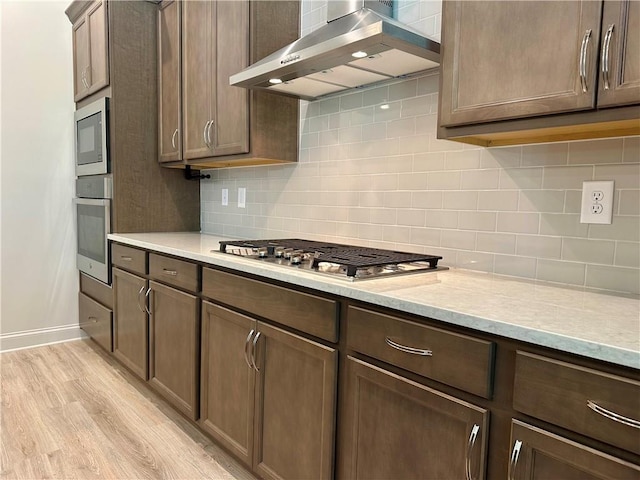 619 Linger Longer Dr, Ellijay, GA 30540 - kitchen featuring wall chimney exhaust hood, stainless steel appliances, light wood-style flooring, tasteful backsplash, and dark brown cabinets