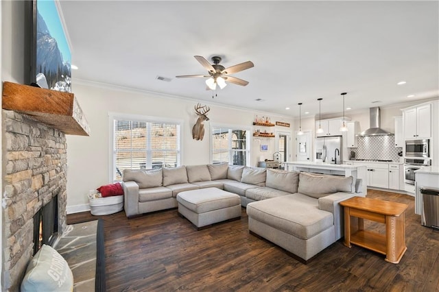 living area with a stone fireplace, dark wood-type flooring, visible vents, and crown molding