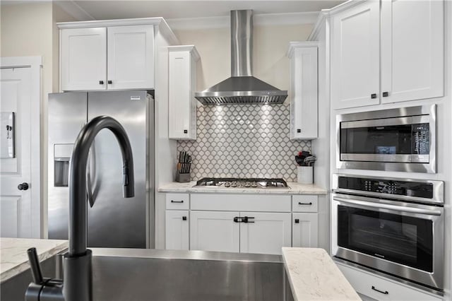 kitchen with light stone counters, white cabinetry, appliances with stainless steel finishes, wall chimney range hood, and backsplash