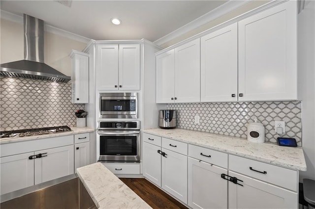 kitchen featuring white cabinetry, wall chimney range hood, appliances with stainless steel finishes, decorative backsplash, and light stone countertops