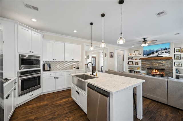 kitchen with stainless steel appliances, a stone fireplace, a sink, and visible vents