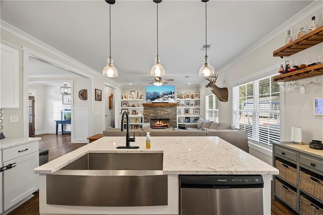 kitchen featuring hanging light fixtures, stainless steel dishwasher, ornamental molding, a sink, and a stone fireplace