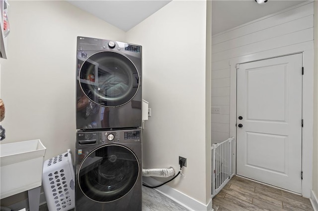 laundry room with a sink, laundry area, stacked washer / dryer, and wood finished floors