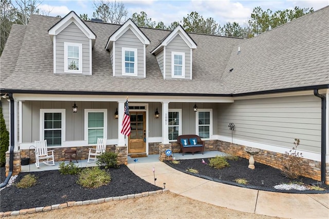 cape cod house with stone siding, a porch, and a shingled roof