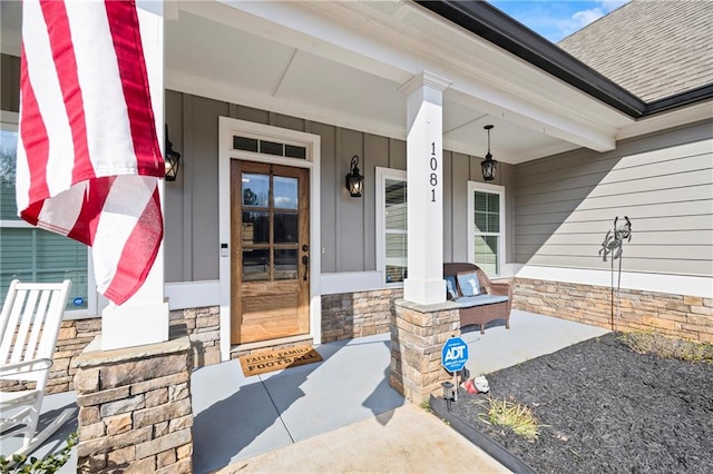 entrance to property with covered porch, stone siding, and roof with shingles