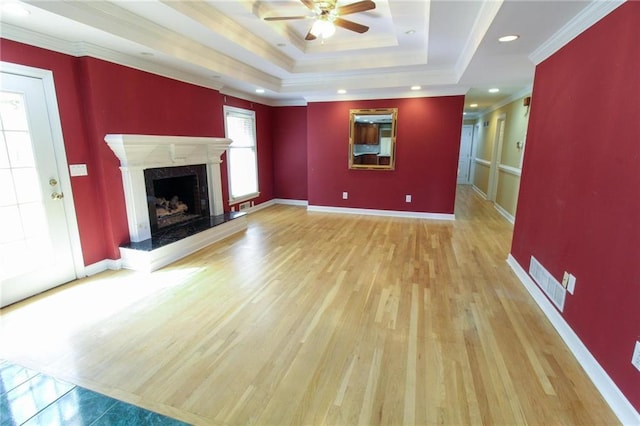 unfurnished living room featuring a tray ceiling, crown molding, light wood finished floors, visible vents, and a premium fireplace