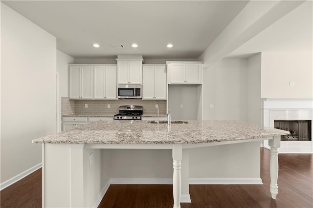 kitchen with sink, white cabinetry, light stone counters, a large island with sink, and stainless steel appliances