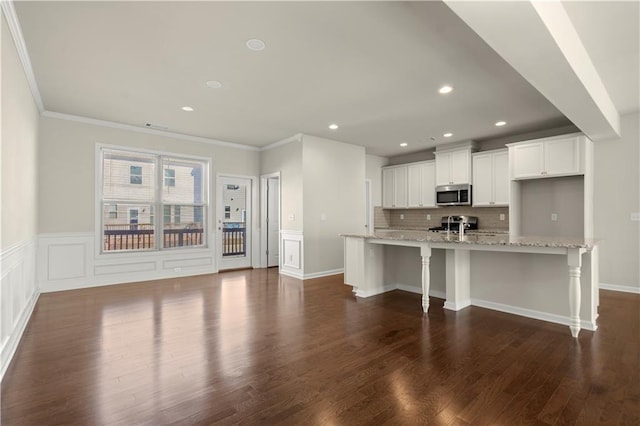 kitchen with a breakfast bar, white cabinetry, light stone counters, a large island with sink, and appliances with stainless steel finishes