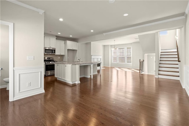 kitchen featuring appliances with stainless steel finishes, dark hardwood / wood-style floors, white cabinetry, an island with sink, and light stone counters