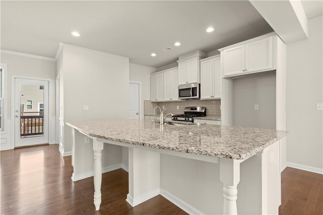 kitchen with white cabinetry, stainless steel appliances, light stone counters, and a large island with sink