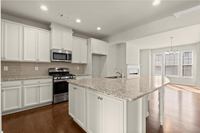 kitchen featuring light stone counters, appliances with stainless steel finishes, a kitchen island with sink, and white cabinets