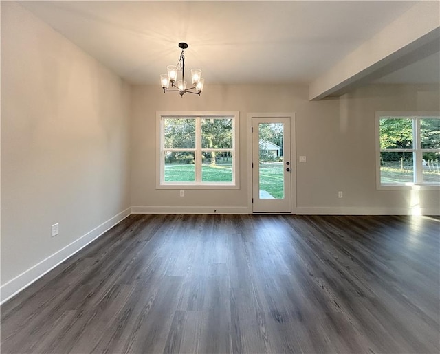 empty room featuring a wealth of natural light, a notable chandelier, and dark hardwood / wood-style flooring