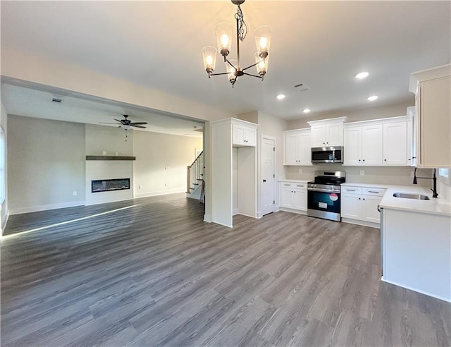 kitchen with sink, appliances with stainless steel finishes, white cabinetry, hardwood / wood-style floors, and ceiling fan with notable chandelier