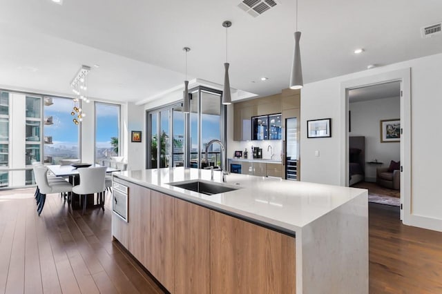 kitchen featuring pendant lighting, dark hardwood / wood-style floors, sink, and an island with sink