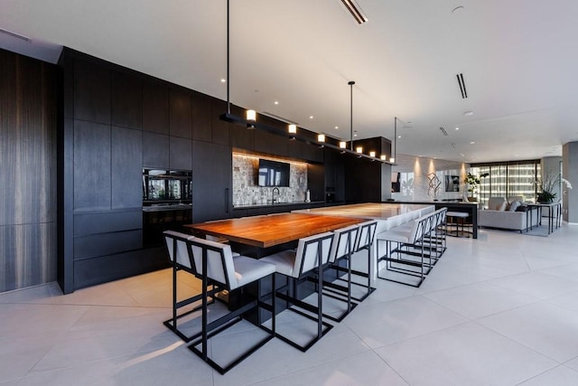 kitchen featuring wood counters, a kitchen breakfast bar, sink, decorative light fixtures, and light tile patterned flooring