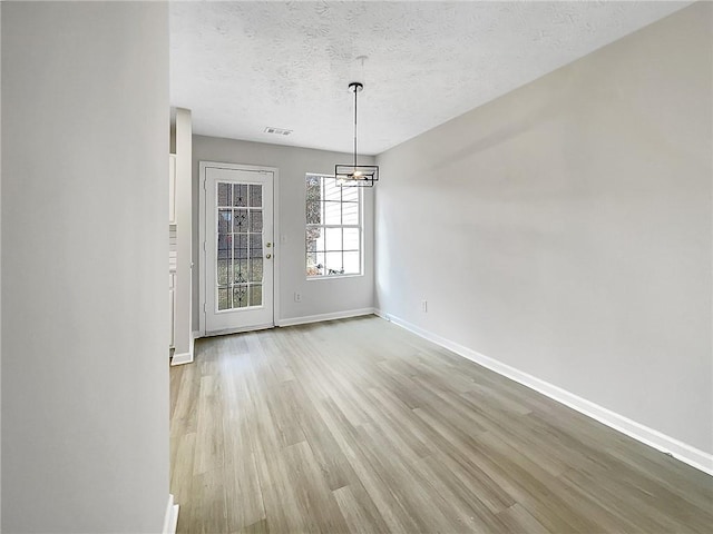 unfurnished dining area with light hardwood / wood-style flooring, a textured ceiling, and an inviting chandelier