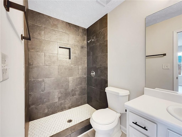 bathroom with tiled shower, vanity, a textured ceiling, and toilet