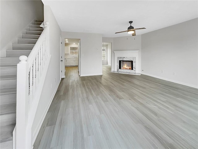 unfurnished living room featuring a high end fireplace, light hardwood / wood-style flooring, and ceiling fan